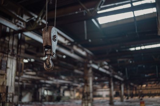 A detailed view of an industrial metal hook hanging inside a rustic warehouse.