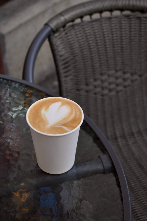 Free Close-up of cappuccino with latte art in paper cup on outdoor table. Stock Photo