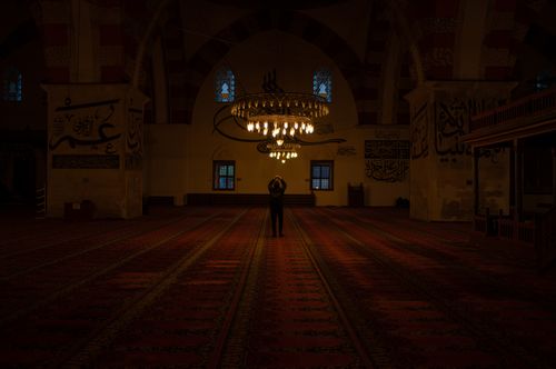 Free A lone figure stands under an illuminated chandelier in a majestic mosque interior, exuding serenity. Stock Photo