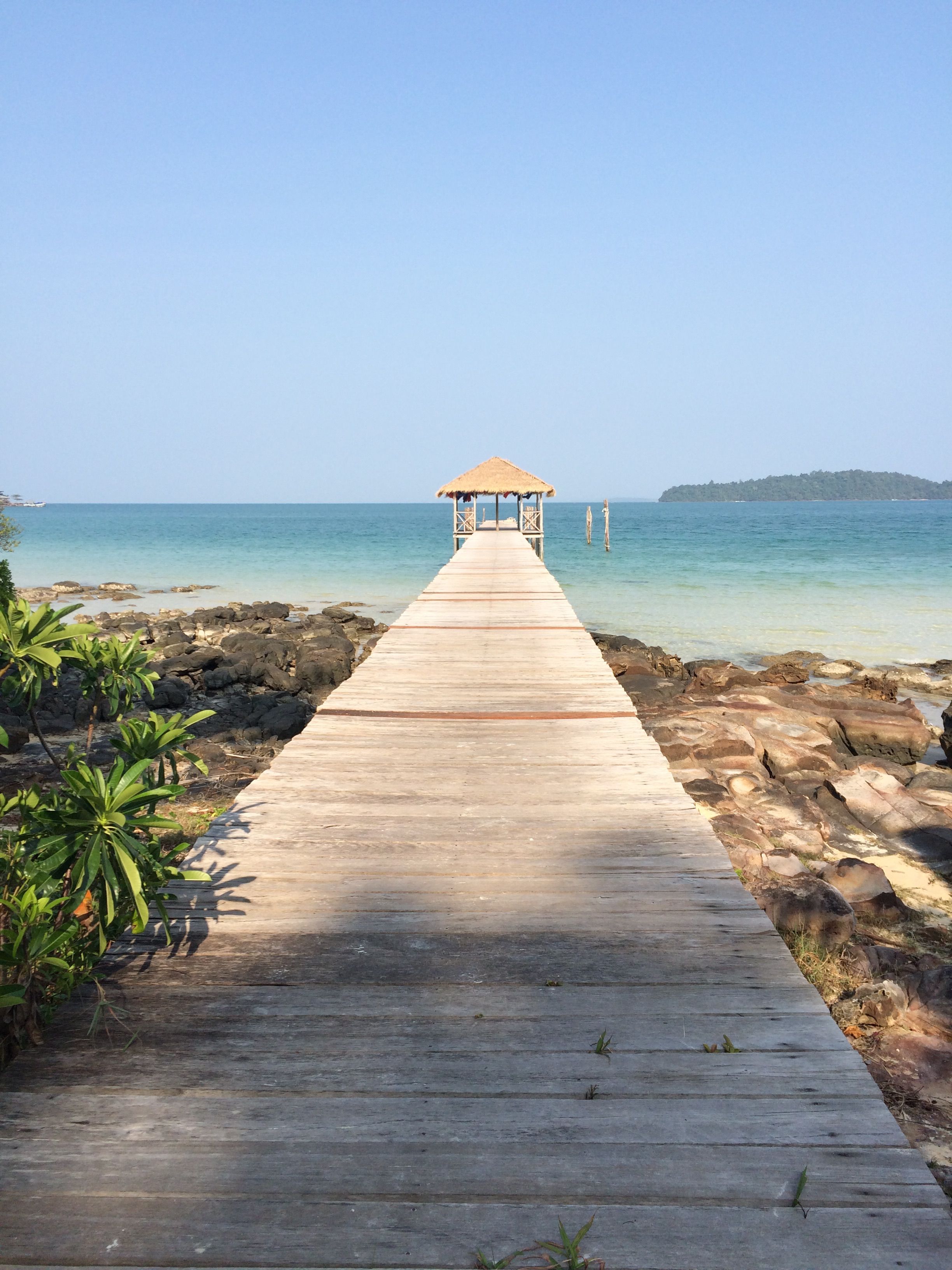 Serene view of a wooden pier stretching toward the tranquil sea under a clear sky.