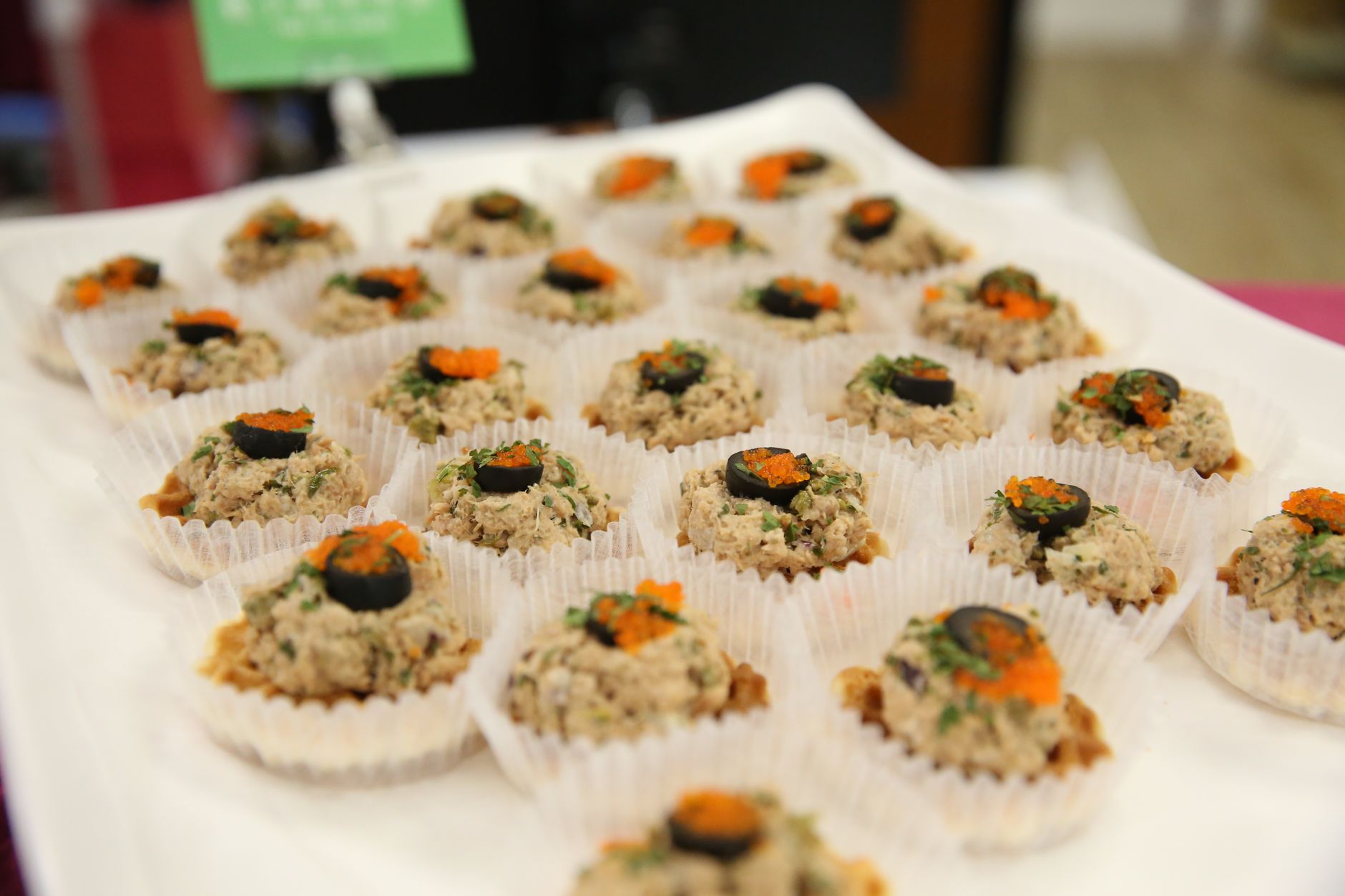 Delicious gourmet appetizers topped with olives and herbs on display in a catering setup.