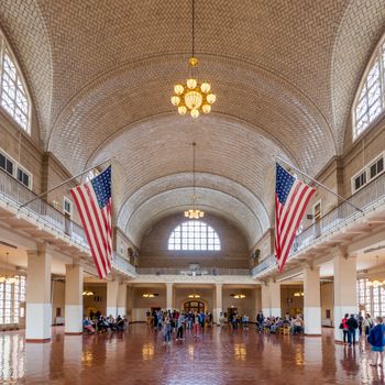 Interior view of Ellis Island's Great Hall featuring American flags and visitors.（イメージ）