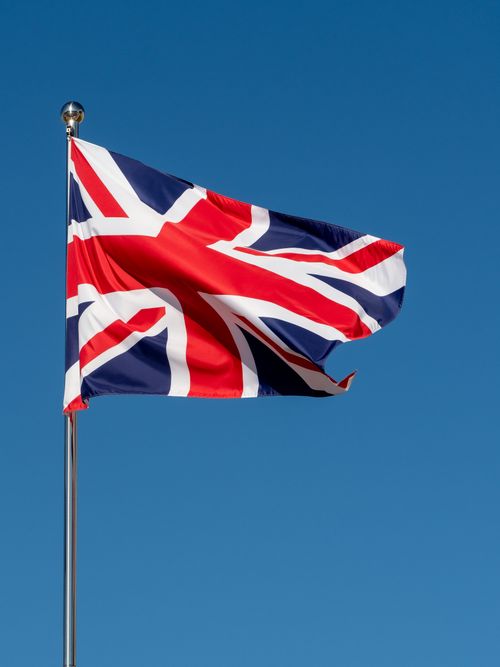 Free Union Jack flag waving on a flagpole against a clear blue sky, symbolizing British patriotism and freedom. Stock Photo