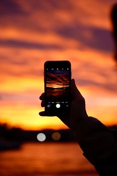 Person photographing a stunning sunset sky with a phone, showcasing vivid colors and serene beauty.