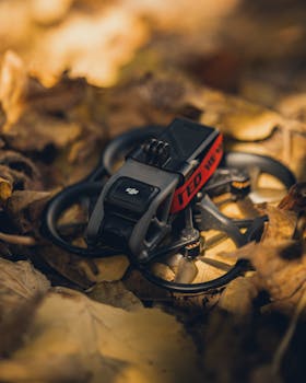 Close-up of a compact drone resting among brown autumn leaves, showcasing its technology.