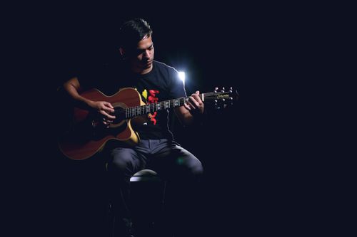 Free Musician playing acoustic guitar in dimly lit studio, focused on stage performance. Stock Photo