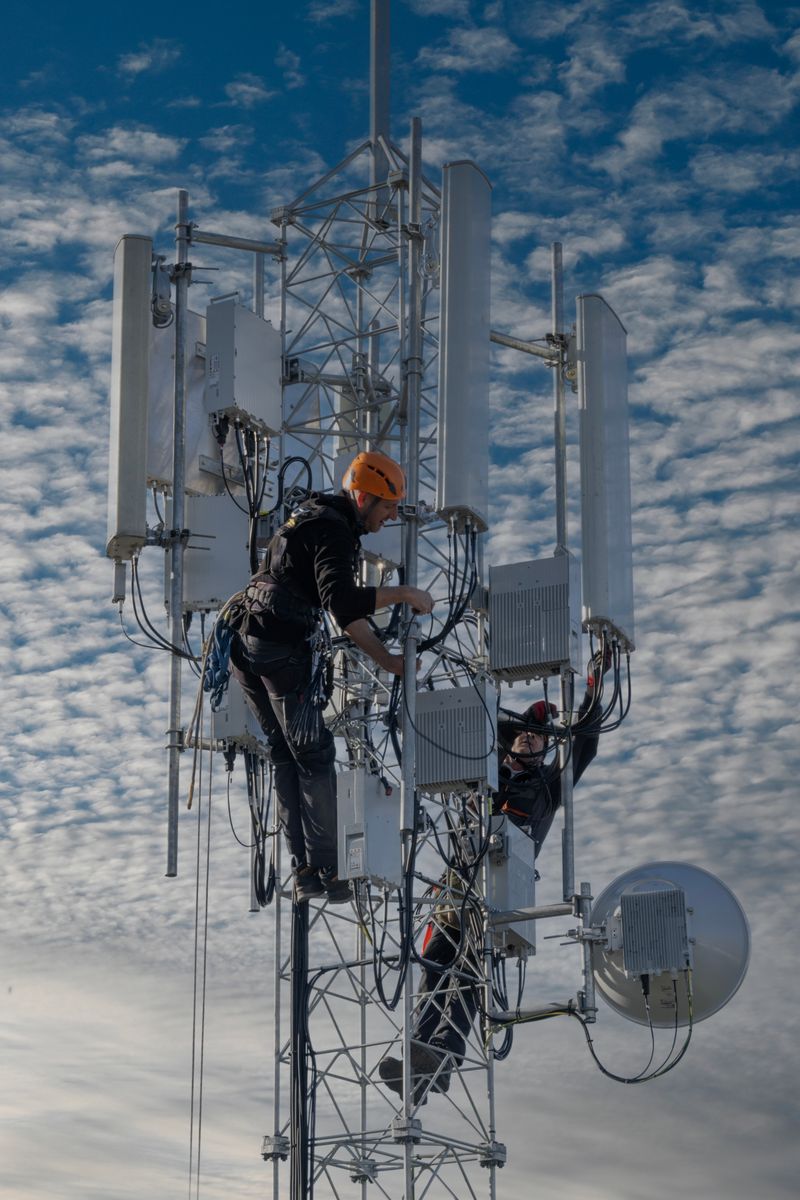 Two technicians working on a cell tower against a cloudy sky, Belgrade.