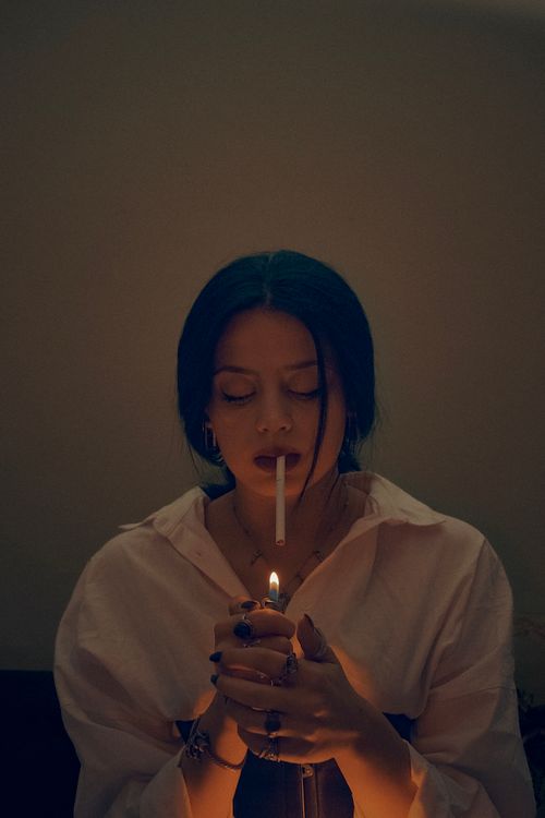 Free A young woman in a white shirt lights a cigarette in a dimly lit room, Ankara, Türkiye. Stock Photo
