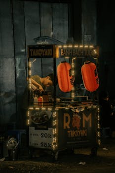 A street vendor prepares Takoyaki under the glow of lanterns at night, showcasing a vibrant city life scene.