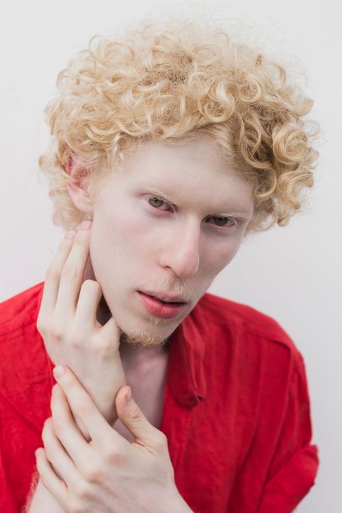 Free Close-up portrait of a person with curly blonde hair in red shirt, posing expressively. Stock Photo