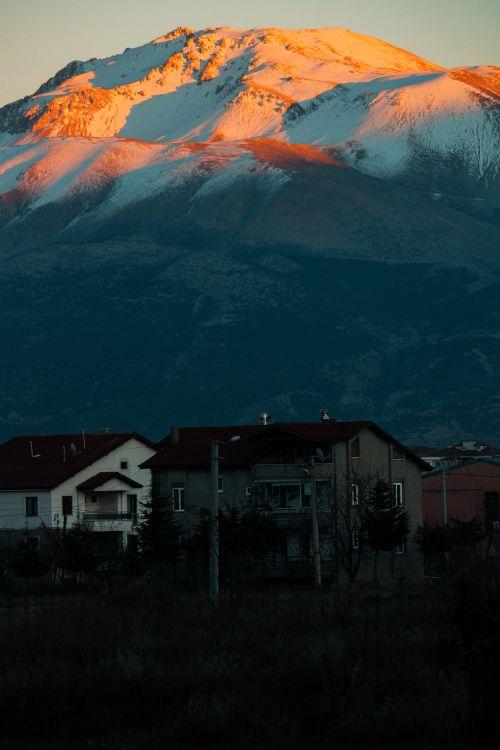 Free Beautiful snowy mountain peaks glowing at sunset with houses in the foreground. Stock Photo
