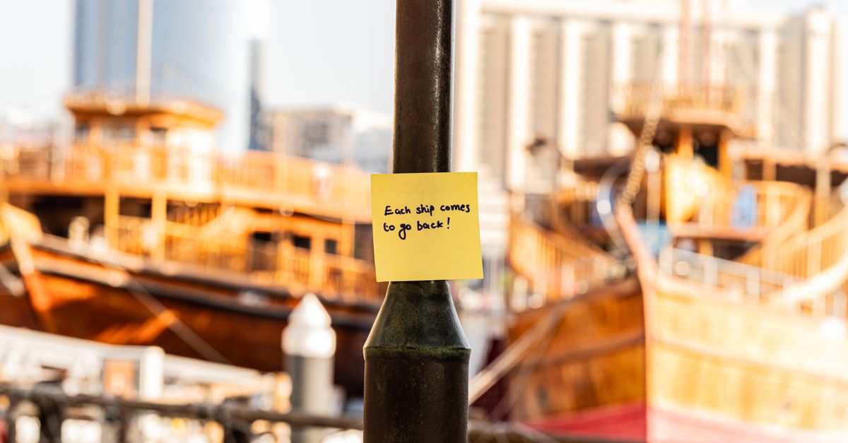 Yellow sticky note with motivational phrase against a backdrop of Dubai Marina's traditional boats.