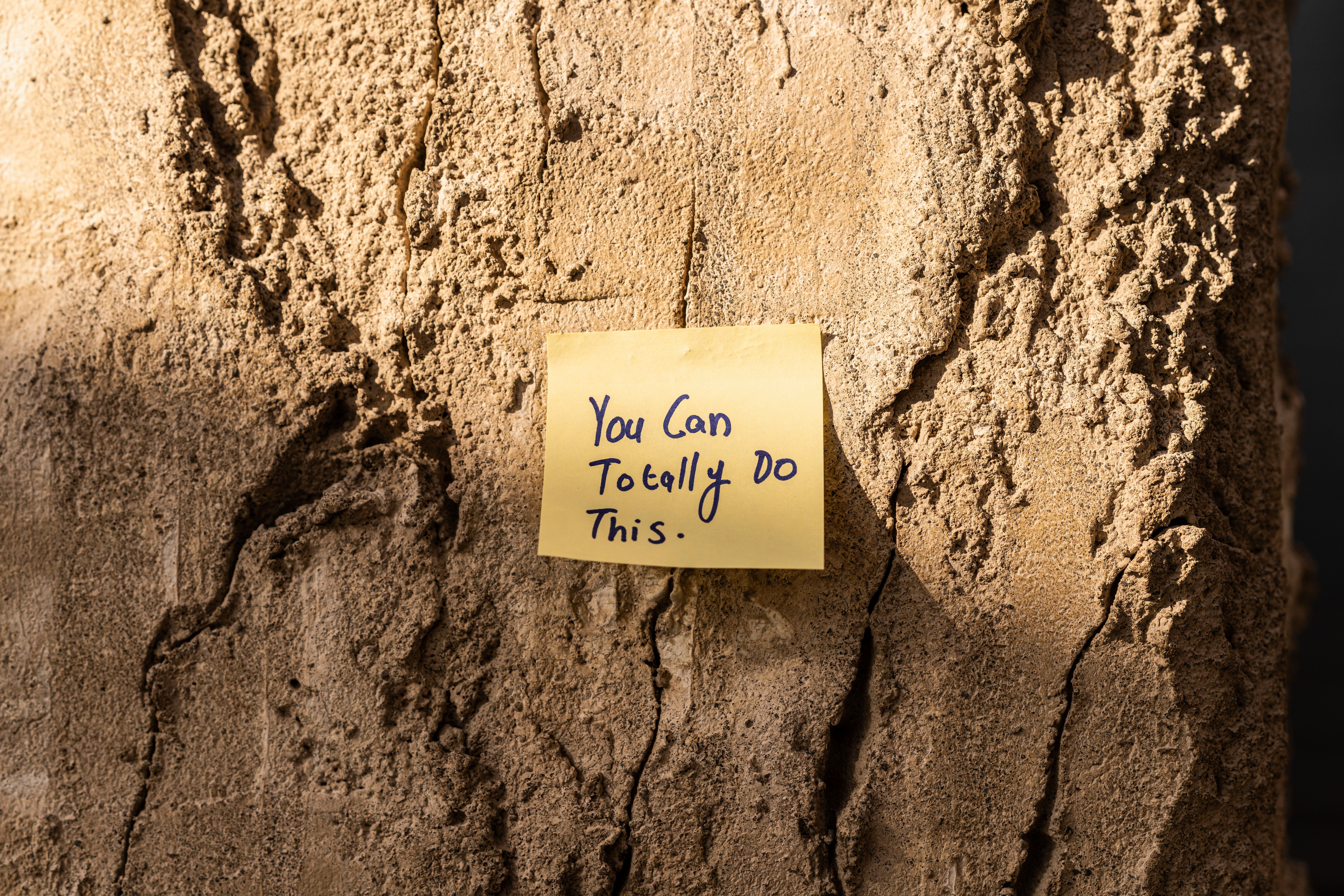 A sticky note with a motivational message on a textured wall in Dubai, with sunlight casting shadows.