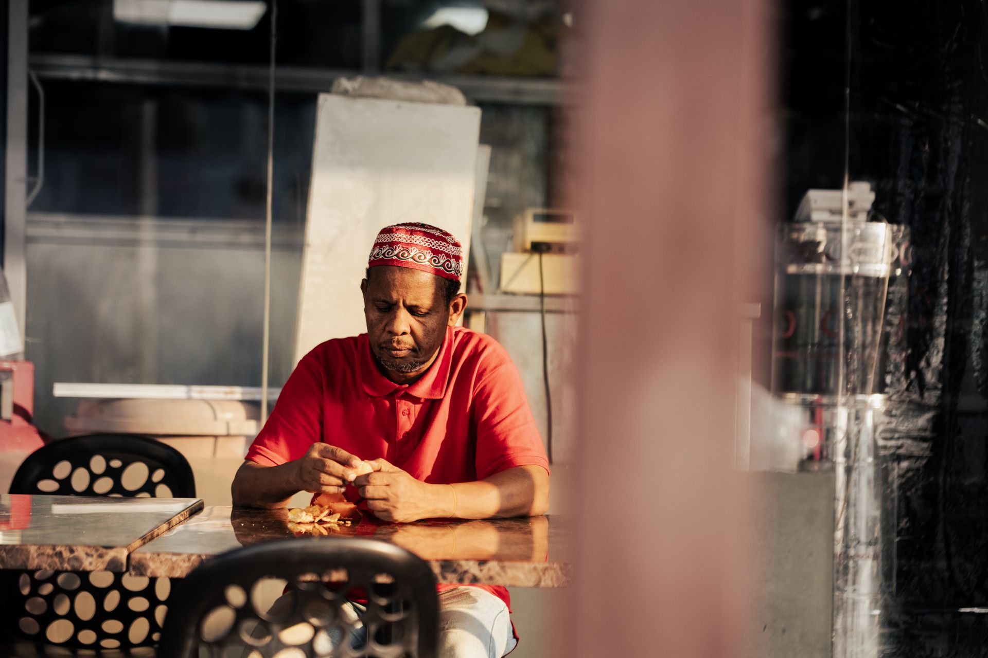 Middle Eastern man in red attire sits at a Dubai market table, reflecting after work.