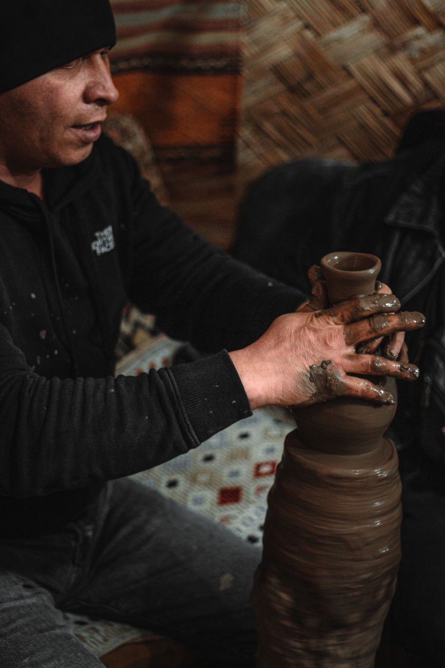 A skilled potter shapes clay on a pottery wheel, creating a ceramic container indoors.