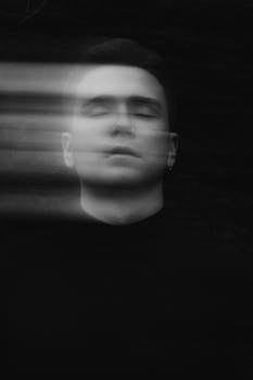 A moody black and white portrait featuring motion blur of a serious man's face in a studio setting.