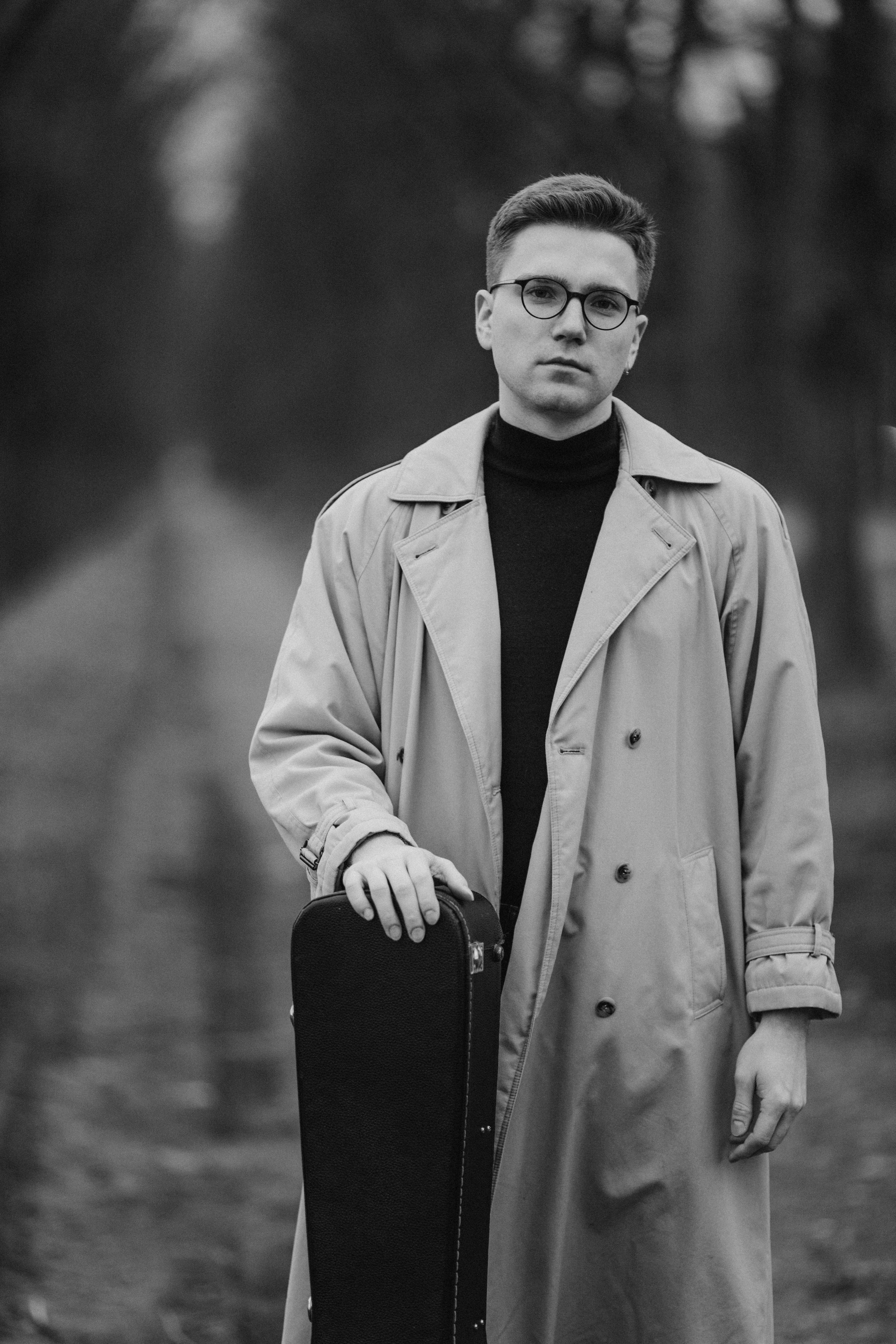 Stylish black and white portrait of a man holding a guitar case on a footpath.