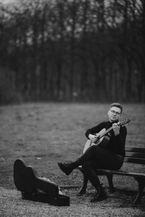 Free A musician playing guitar on a bench in a tranquil meadow, captured in black and white. Stock Photo