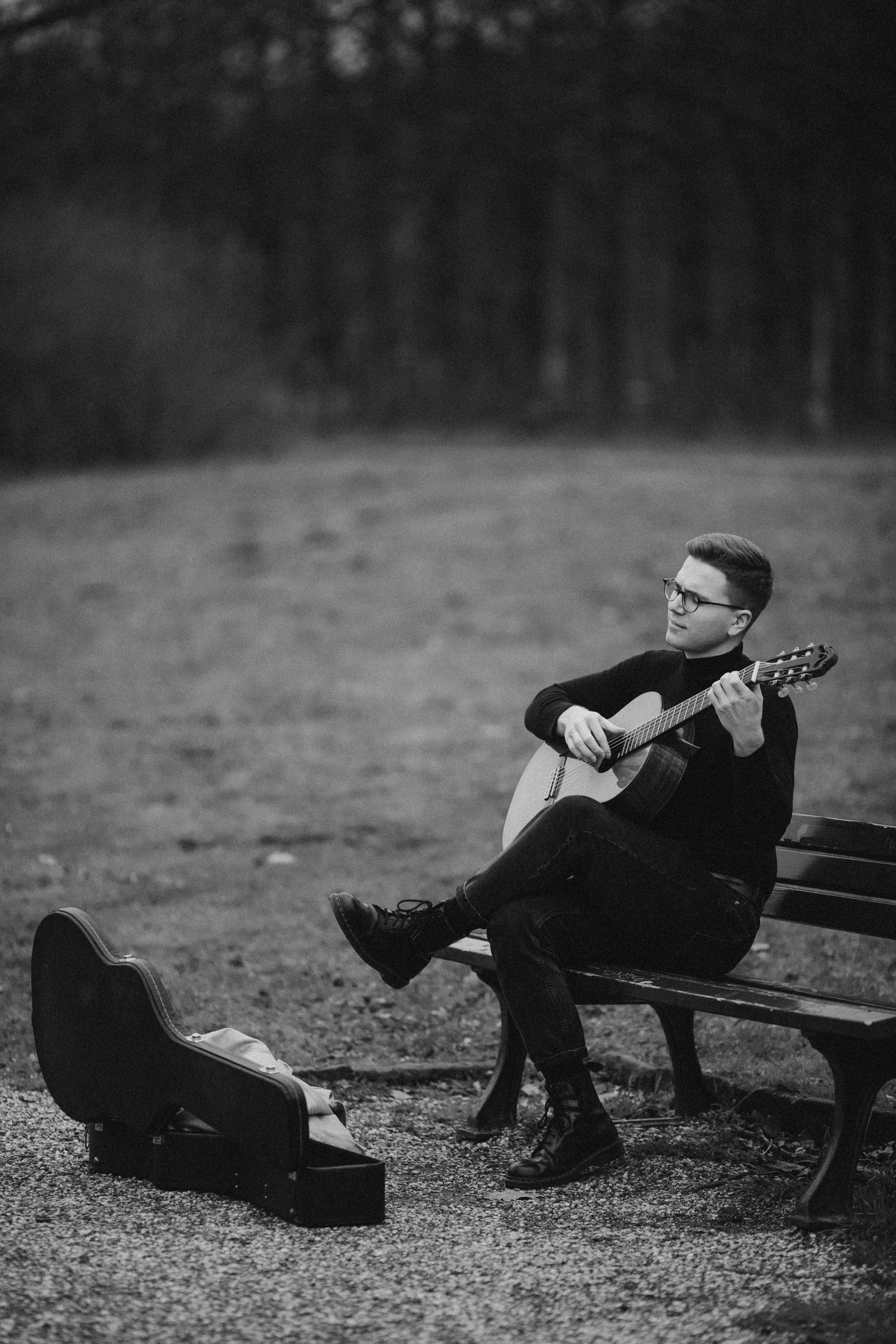 Black and white photo of a man playing guitar on a park bench