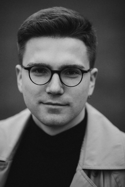 Free Black and white portrait of a young man wearing eyeglasses and a coat, showcasing a contemplative look. Stock Photo