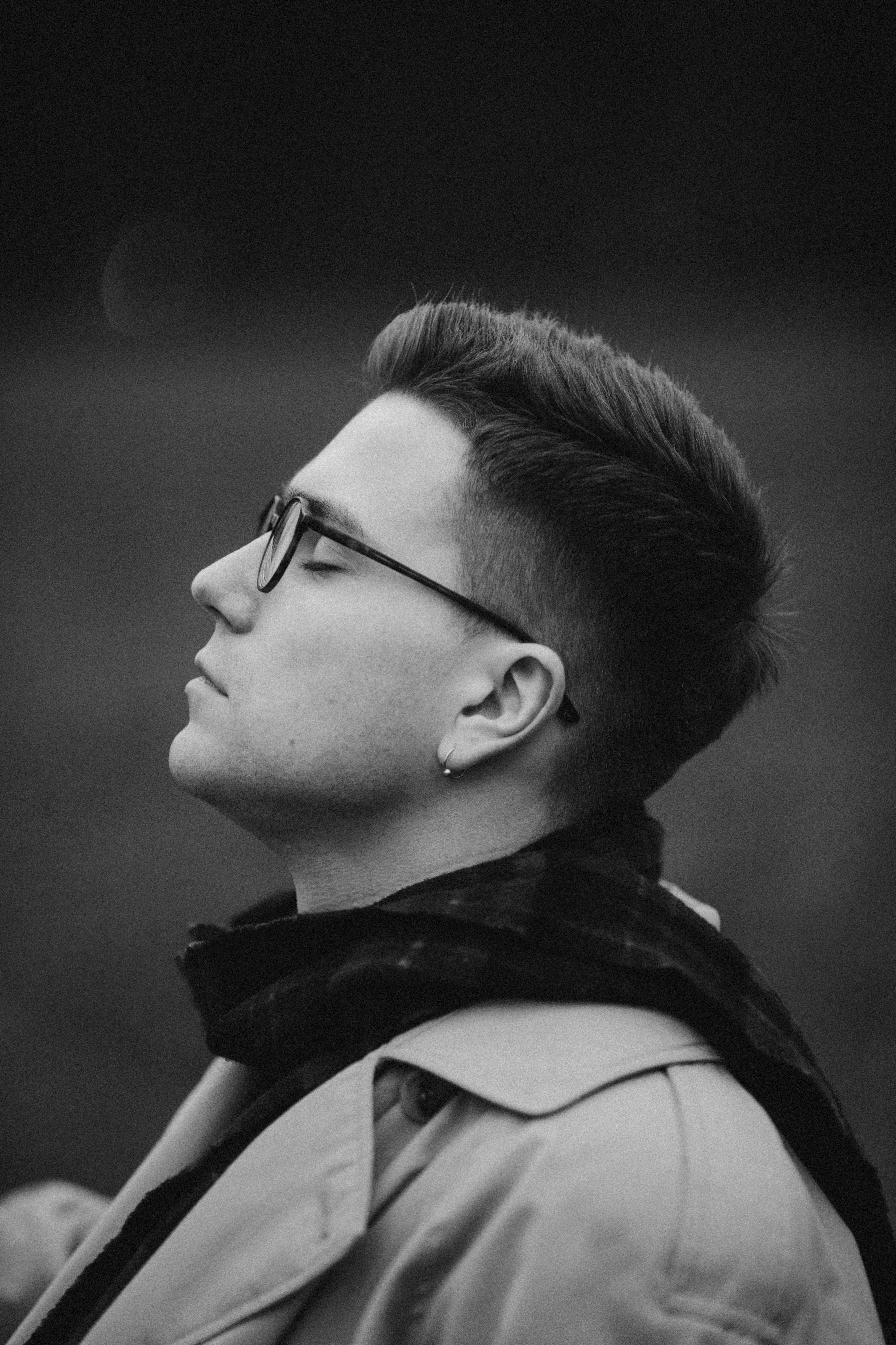 Timeless black and white portrait of a man deep in thought wearing a coat and glasses.