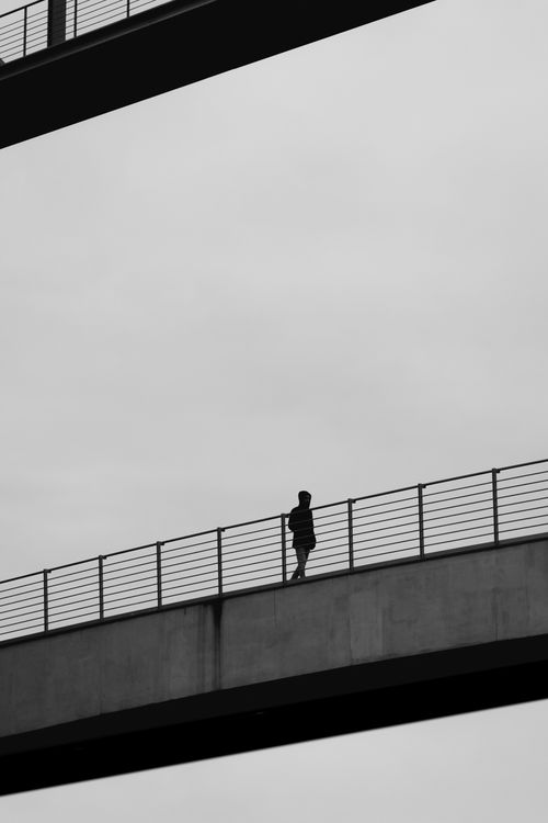 Free A solitary silhouette on a modern bridge against a cloudy sky. Stock Photo