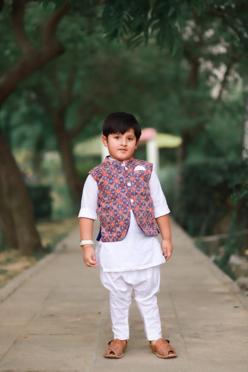 Free A young boy poses in traditional attire amidst a lush park pathway, showcasing cultural elegance. Stock Photo