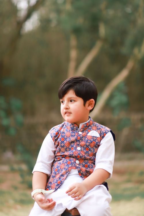 Free A young boy in traditional outfit sitting outdoors, captured in a natural setting. Stock Photo