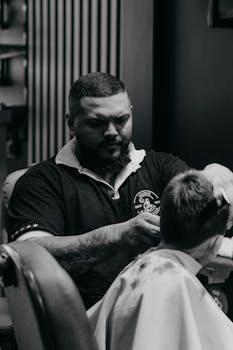 A barber focused on cutting a young boy's hair in a monochrome indoor setting.