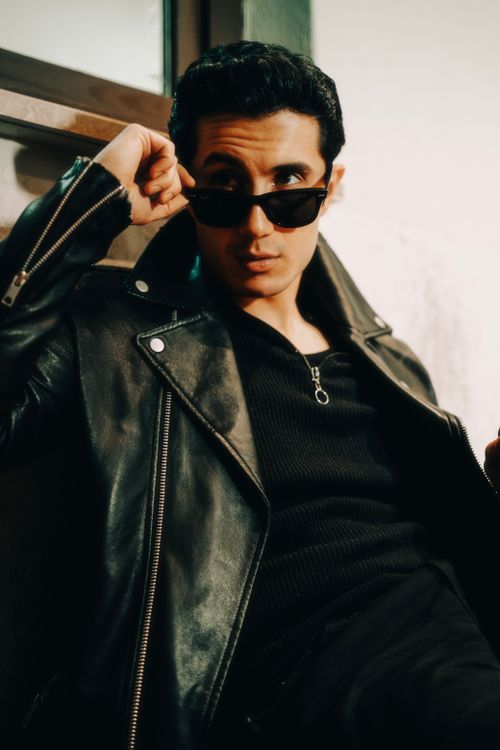 Free A fashionable adult male model posing indoors wearing a leather jacket and sunglasses. Stock Photo