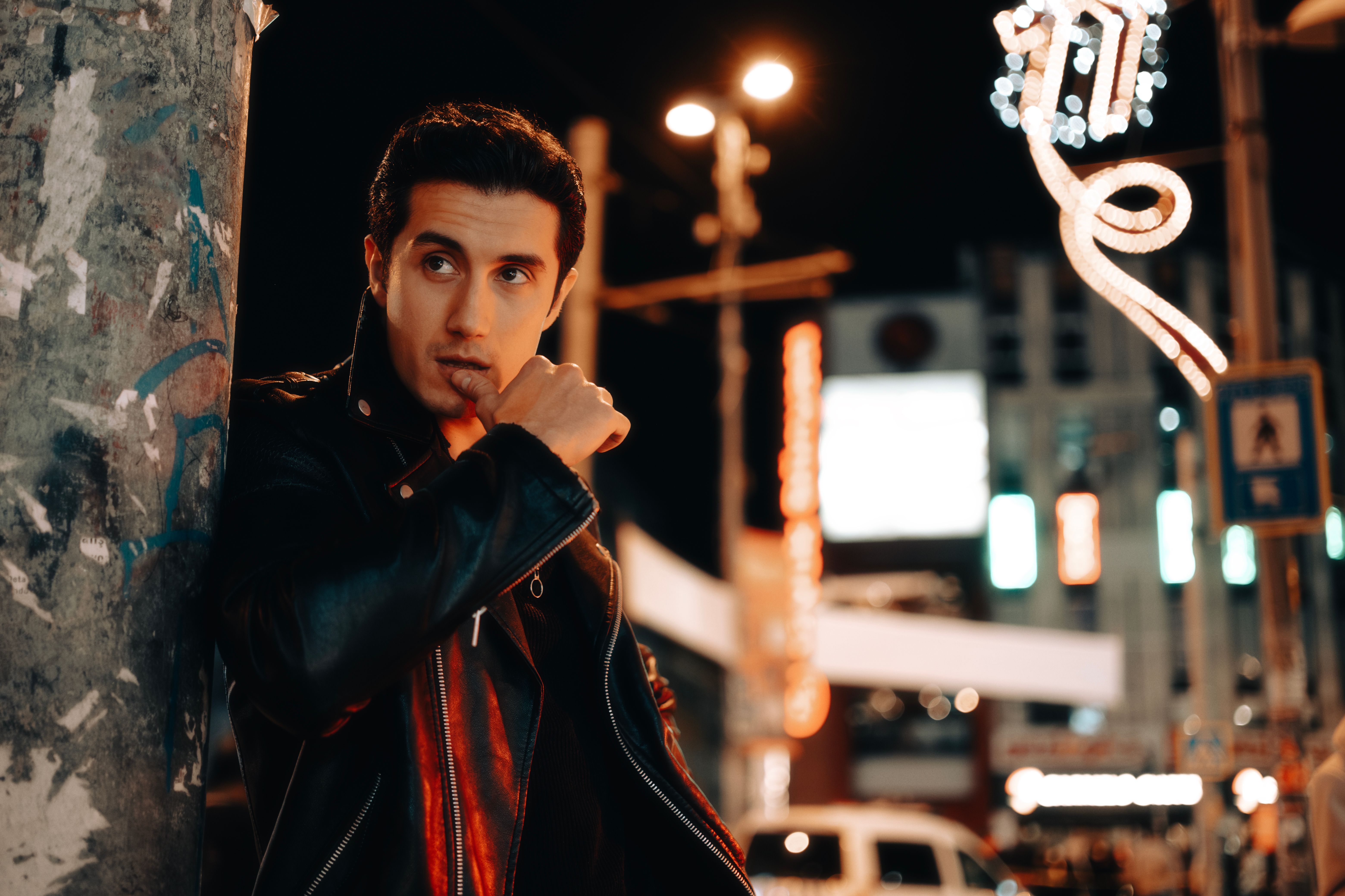 Homme en blouson cuir streetwear élégant dans les lumières de la ville en soirée