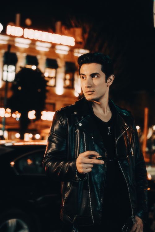 Free Confident man in black leather jacket posing on bustling city street at night. Stock Photo