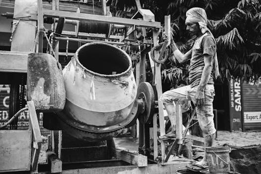 A worker operating a concrete mixer at a construction site in black and white.