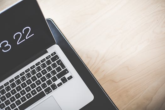 一张浅色木桌上摆放着一个极简主义的工作空间，配备一台笔记本电脑，屏幕亮着显示时间