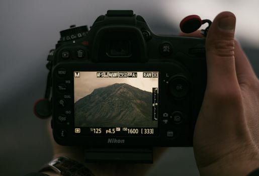 Hands holding a DSLR camera capturing a mountainous landscape