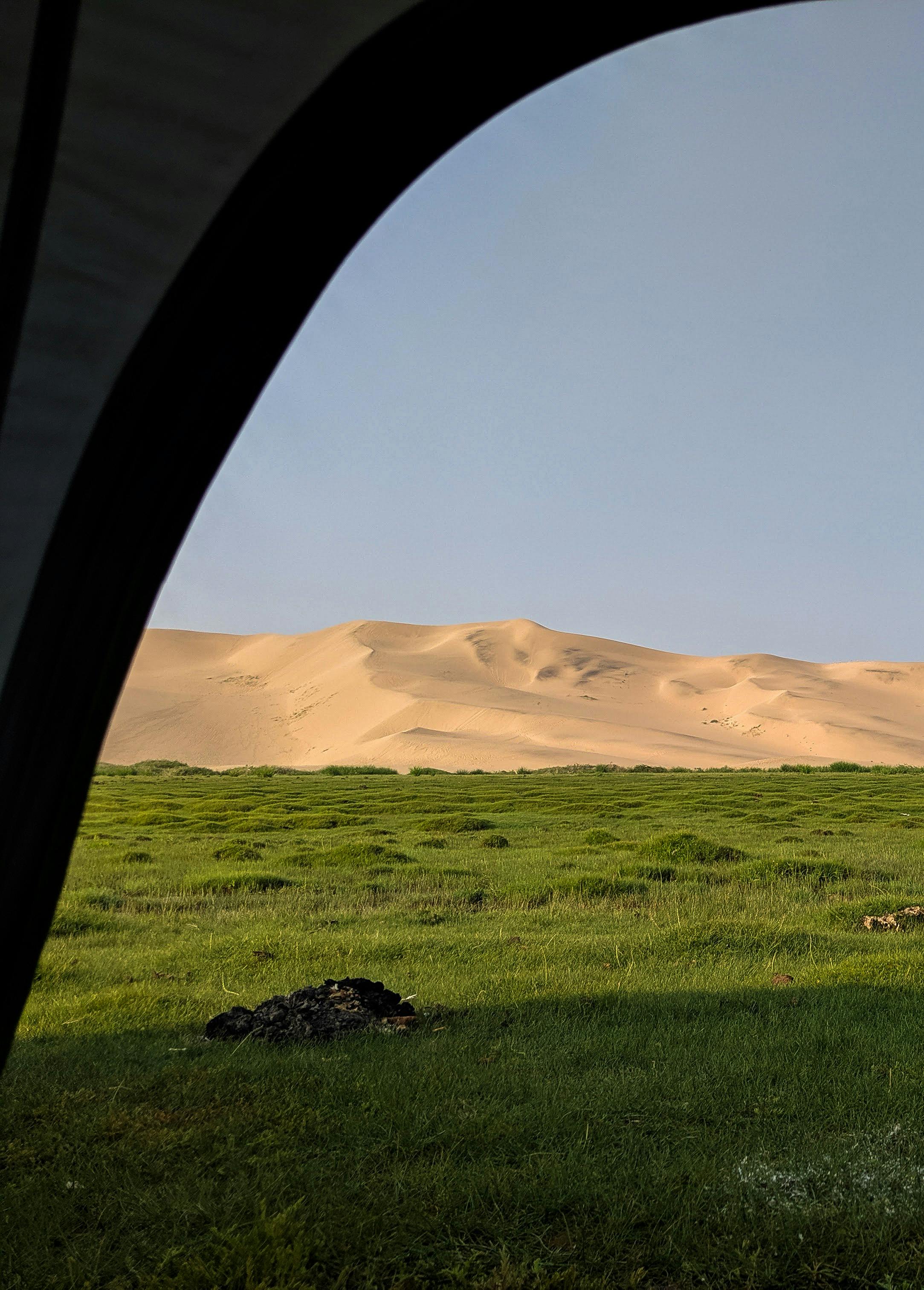 Scenic view of sand dunes and green grassland framed by tent, capturing nature's beauty.