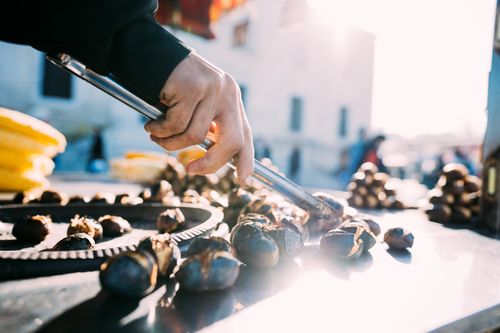 Free Close-up of a street vendor roasting chestnuts with tongs on a sunny day. Vibrant outdoor market scene. Stock Photo