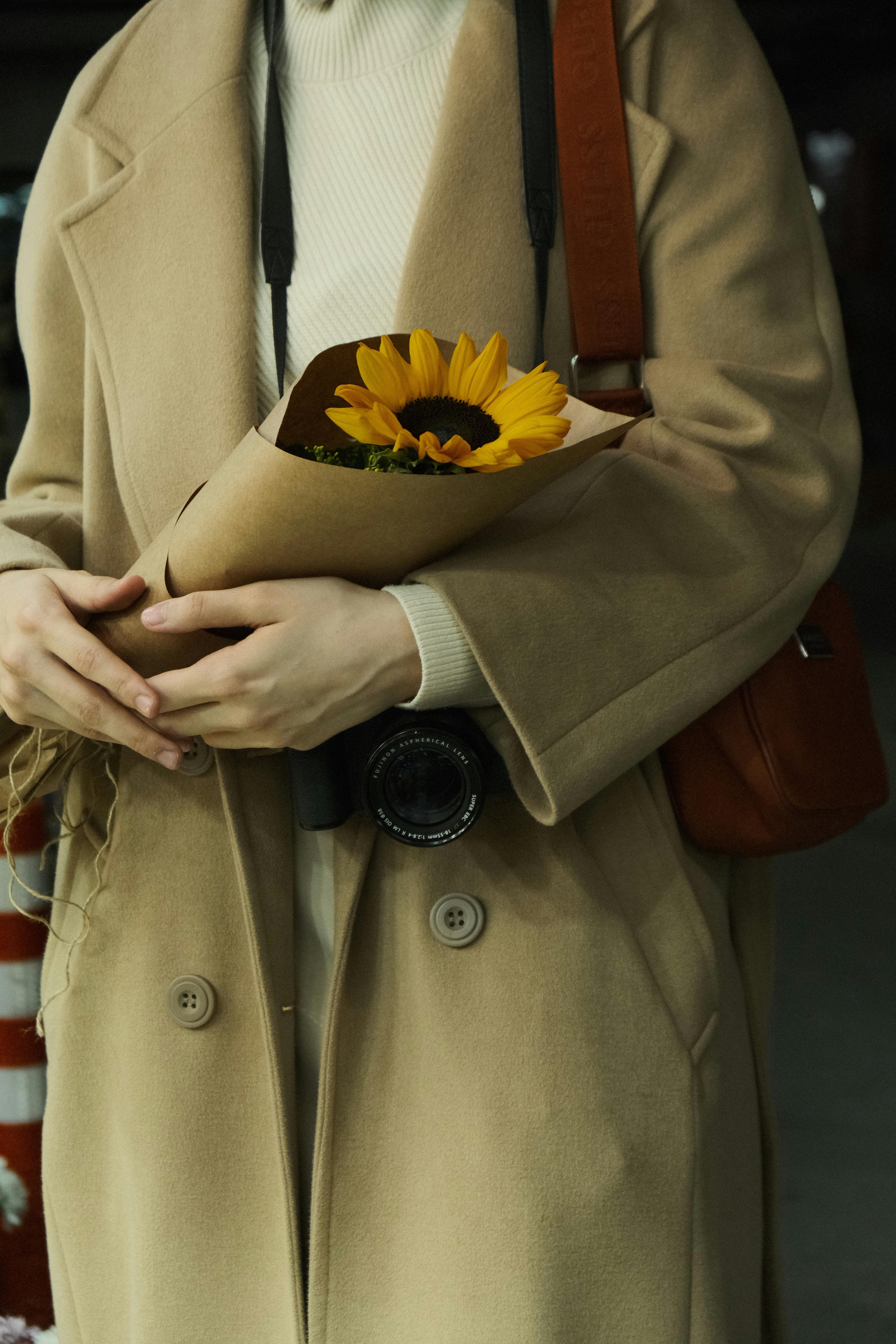 A woman in a trench coat holds a sunflower bouquet, adding a touch of summer elegance.