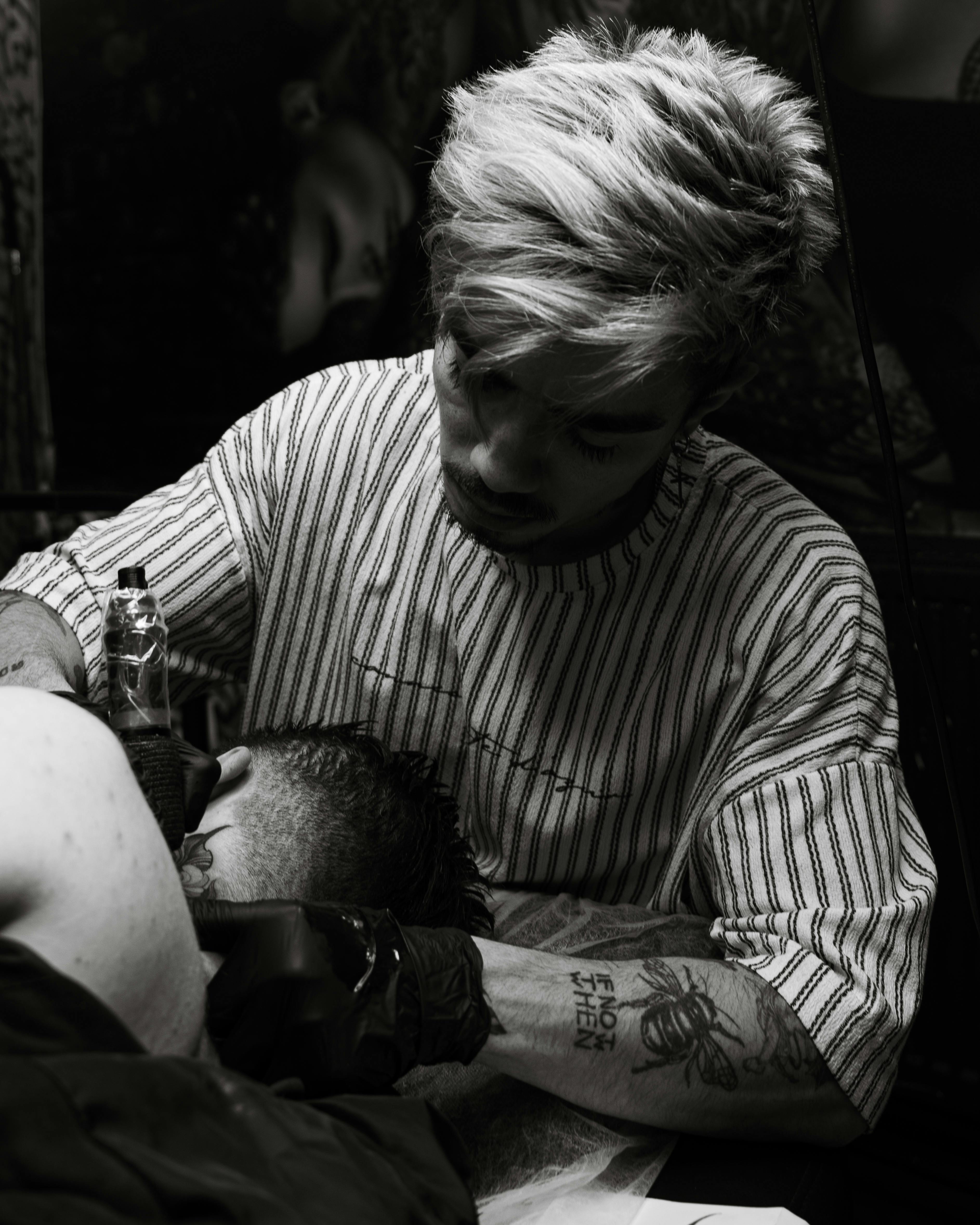 Tattoo artist working on a client in a monochrome tattoo studio.