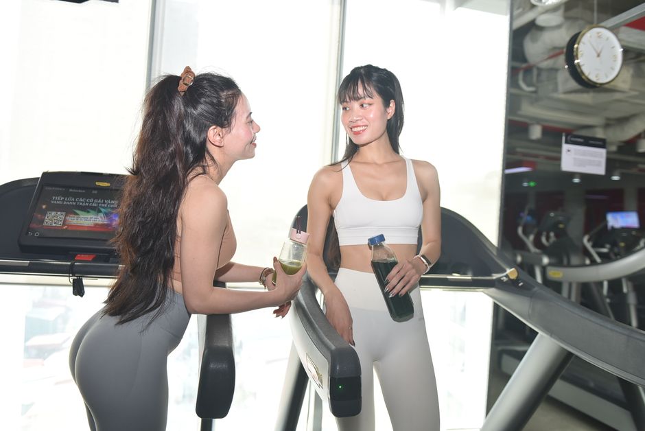 明るいジムの環境でトレッドミルの上にいる二人の女性が会話をしながら微笑んでいます。