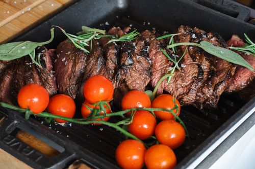 Free Sliced grilled steak accompanied by cherry tomatoes and fresh rosemary in a cast iron pan. Stock Photo