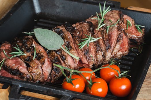 Juicy grilled steak garnished with rosemary and accompanied by fresh cherry tomatoes.