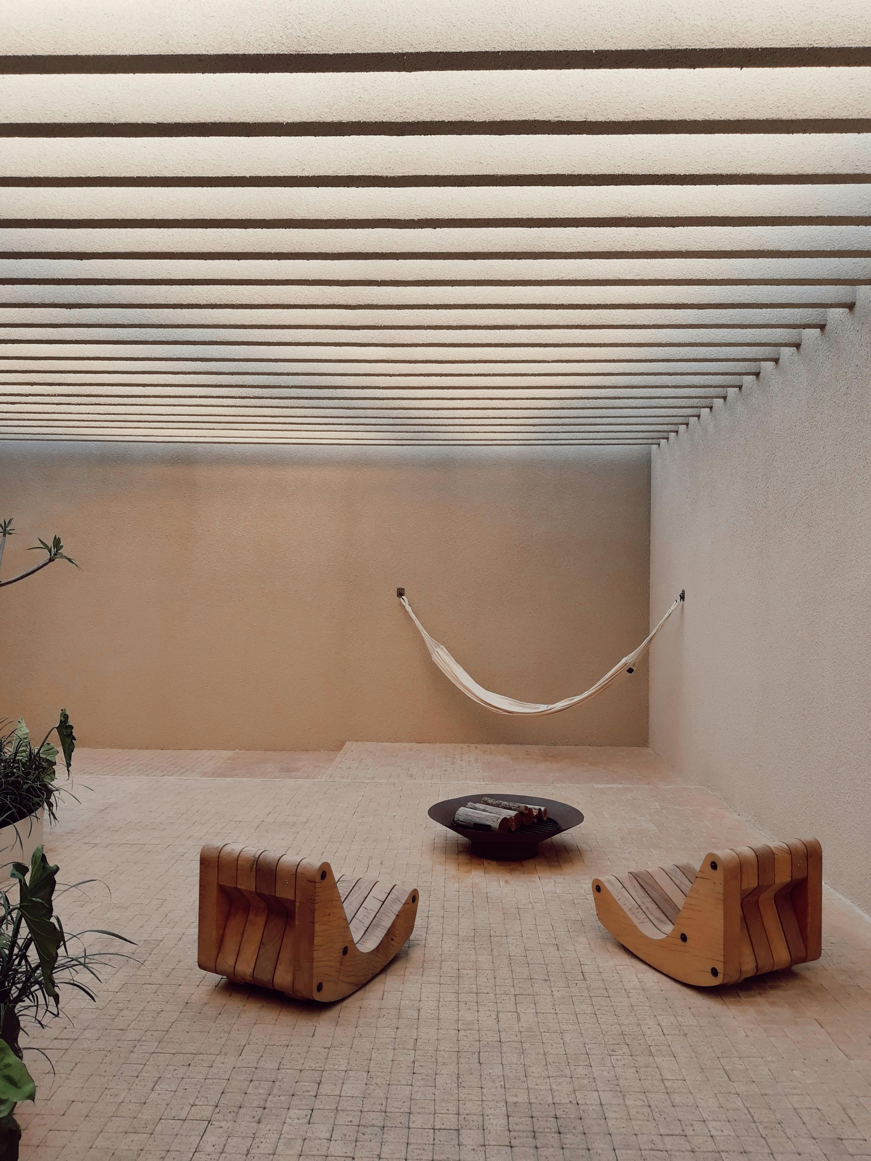 A serene minimalist patio setting with wooden rocking chairs and a suspended hammock.