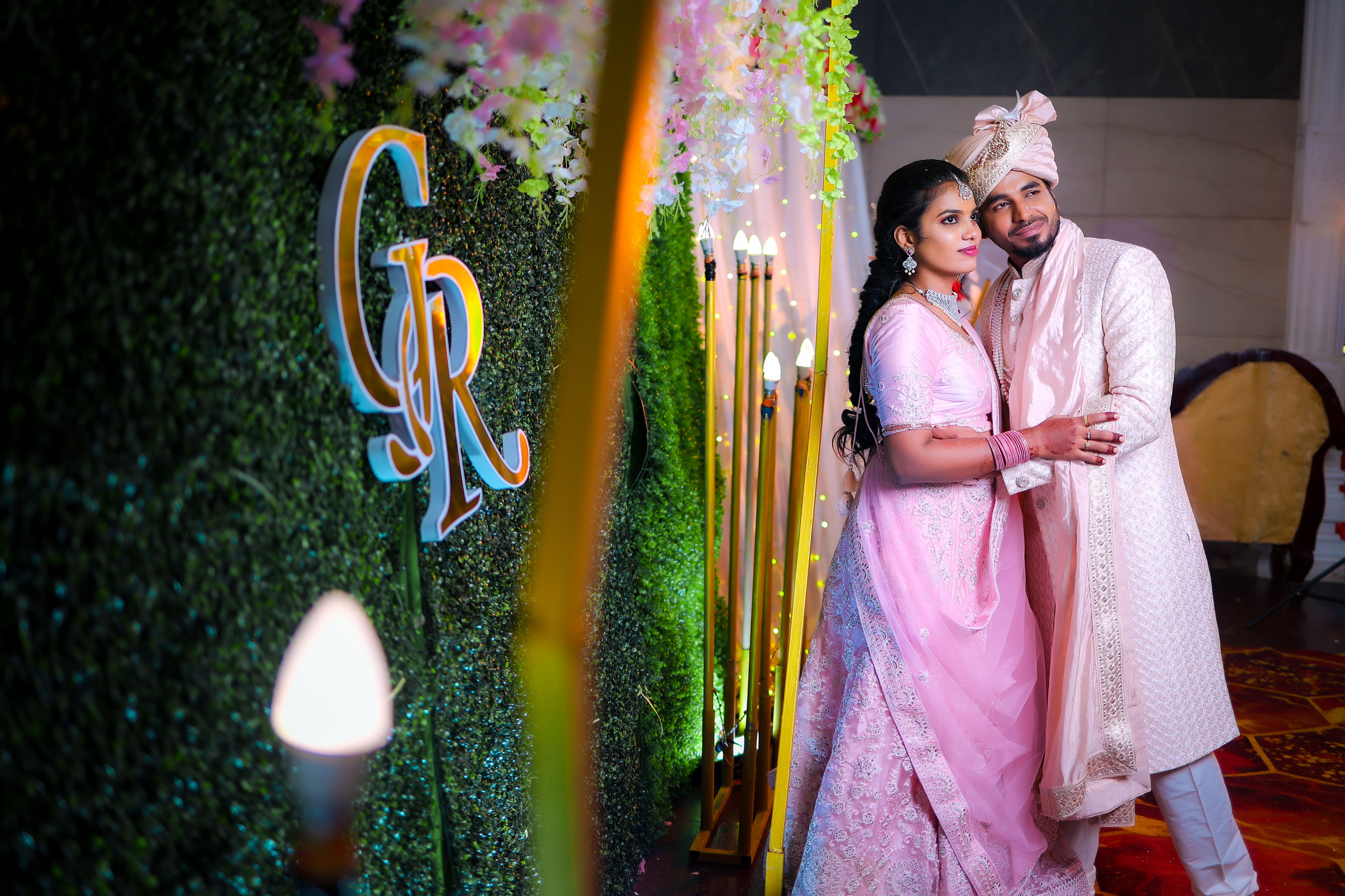 South Asian couple in traditional attire posing happily at an indoor wedding ceremony.