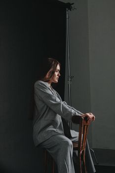 A poised woman in a gray suit elegantly poses on a chair in a studio setting.