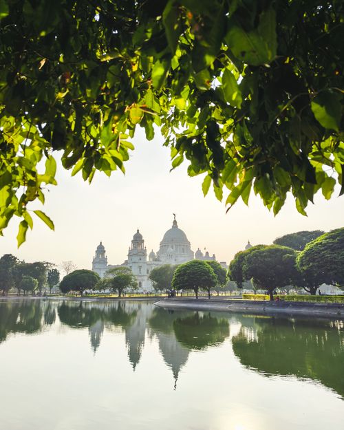 Free Victoria Memorial in Kolkata reflected in serene water with lush green trees. Stock Photo
