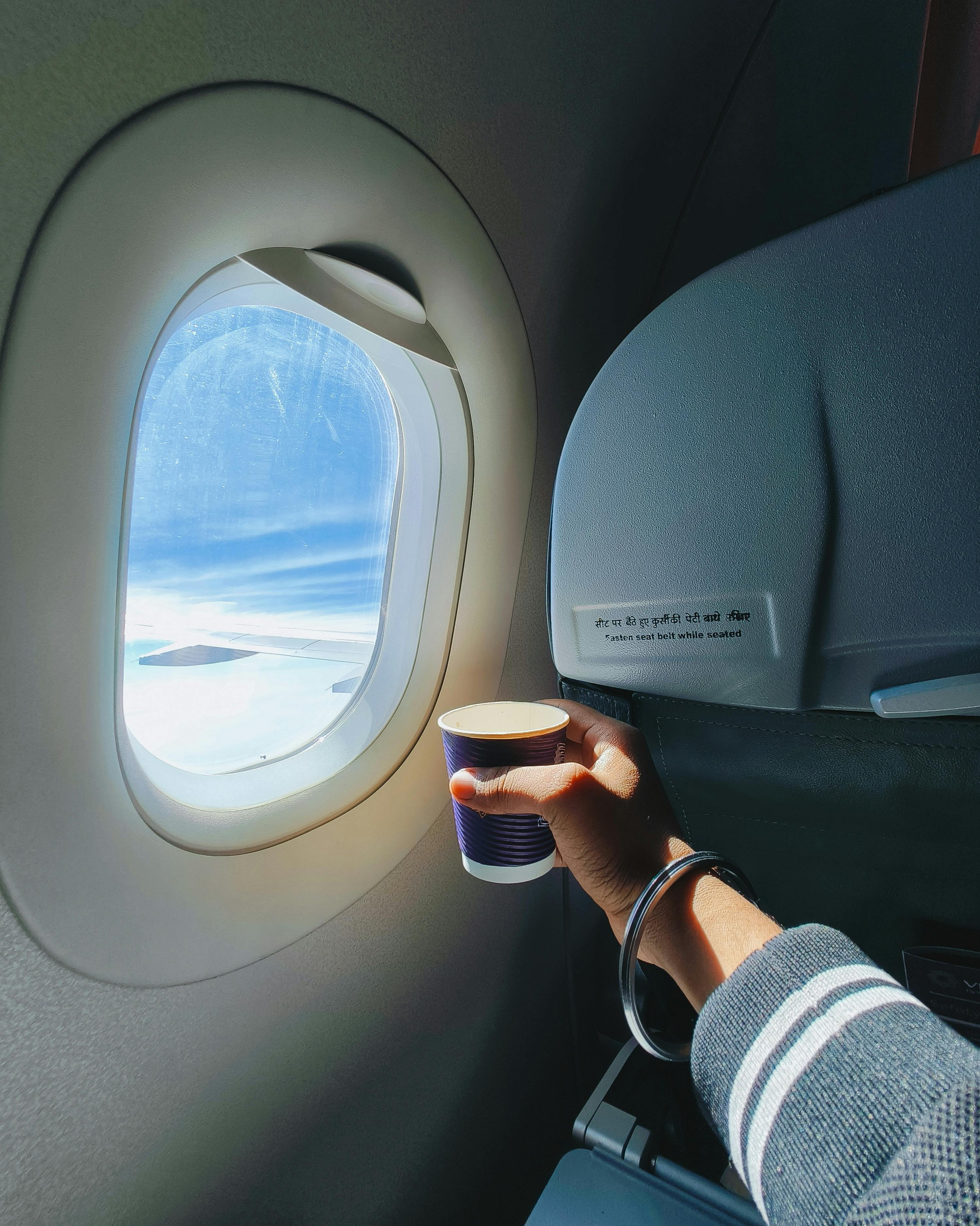 Hand Holding Cup by Window of Flying Airplane · Free Stock Photo