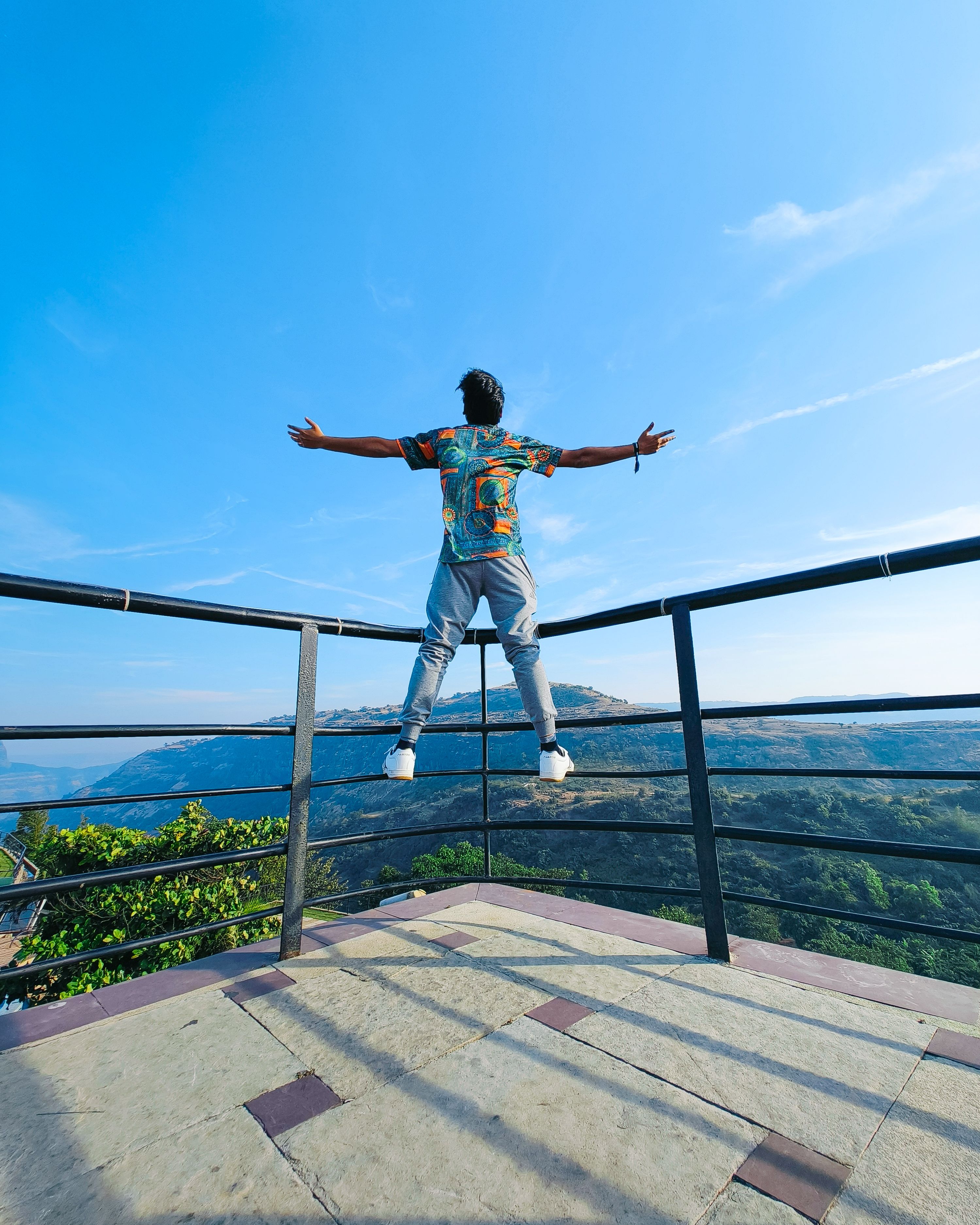 Fotomural Un hombre de pie con alegría en un observatorio en Lonavala, India, abrazando el cielo azul y las montañas.