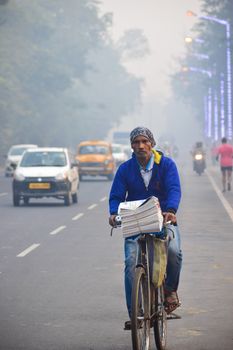 A man delivers newspapers on a bicycle along a misty street in Kolkata, India.