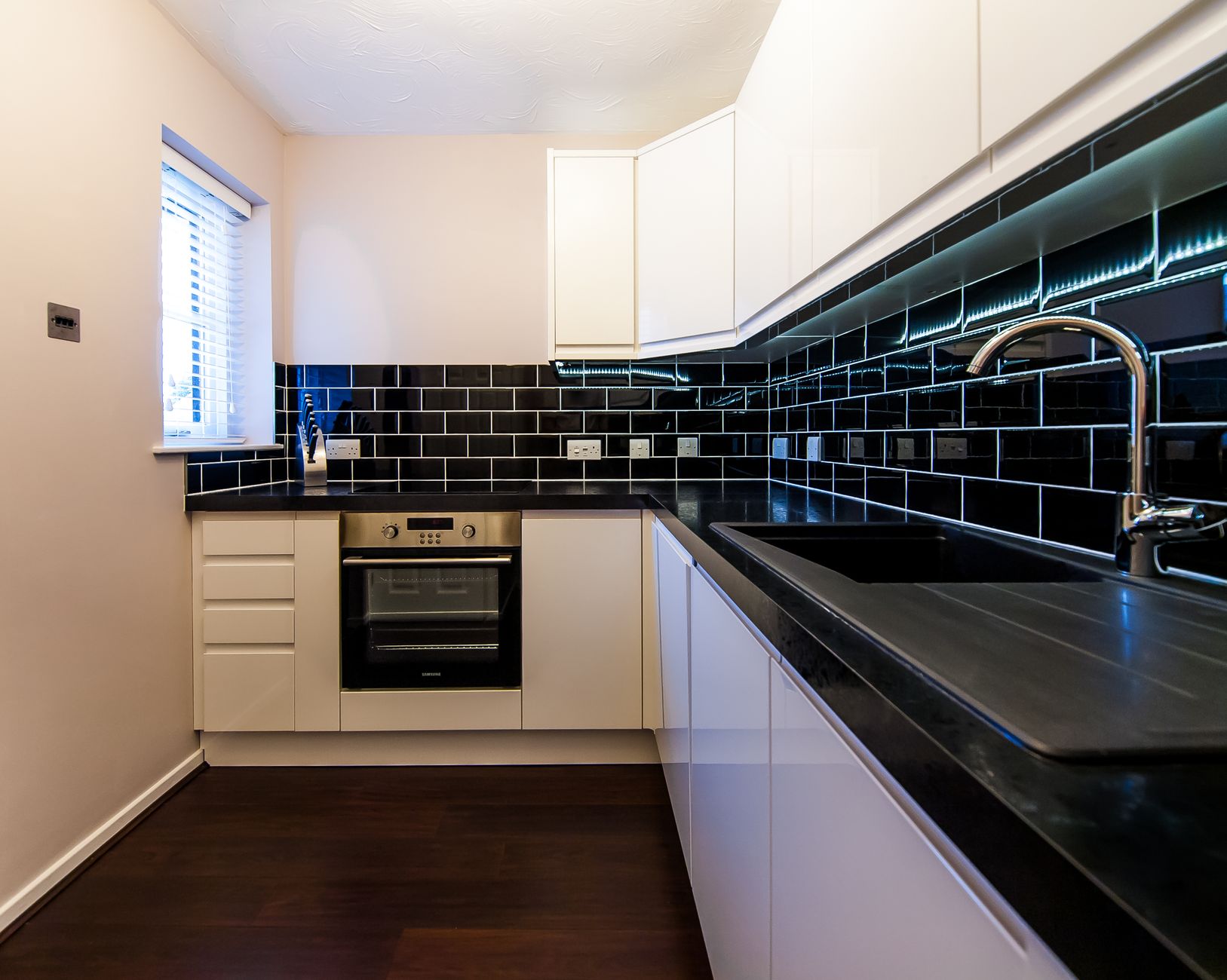 Sleek minimalist London kitchen with black tile backsplash and white flat-panel cabinets, a smart summer resale renovati Sleek minimalist London kitchen with black tile backsplash and white flat-panel cabinets, a smart summer resale renovati